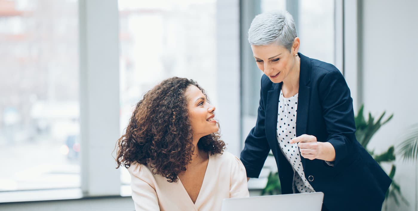 person sitting at a computer talking to a coworker