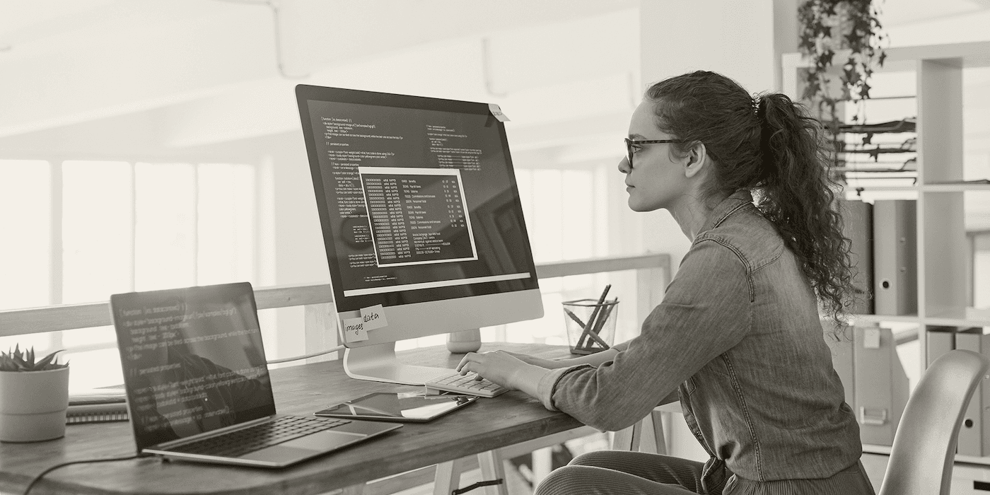 person sitting at a desk typing code on a computer with a monitor and laptop open