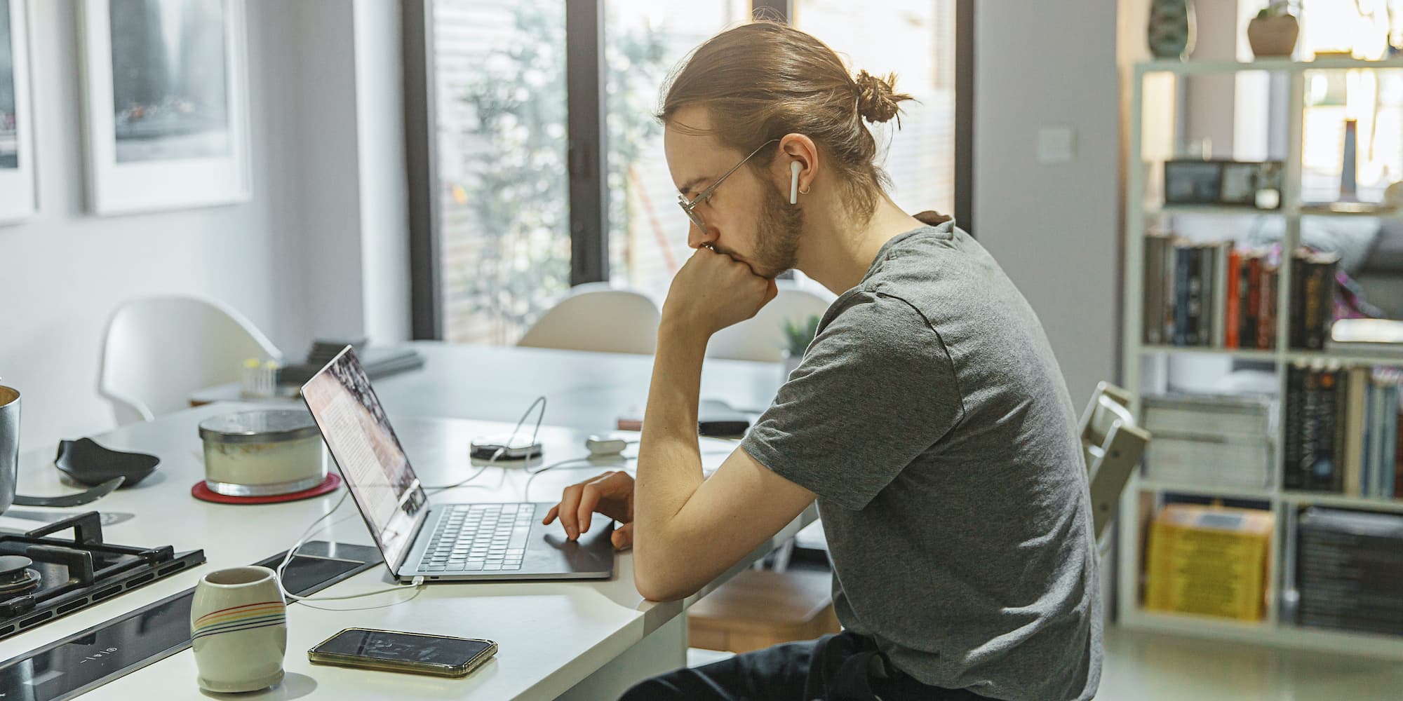 person sitting at kitchen counter with laptop wearing AirPods with phone next to them