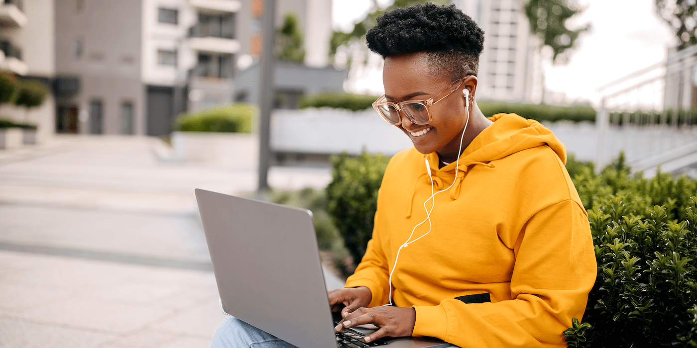 college student sitting outside on campus typing on a laptop and smiling