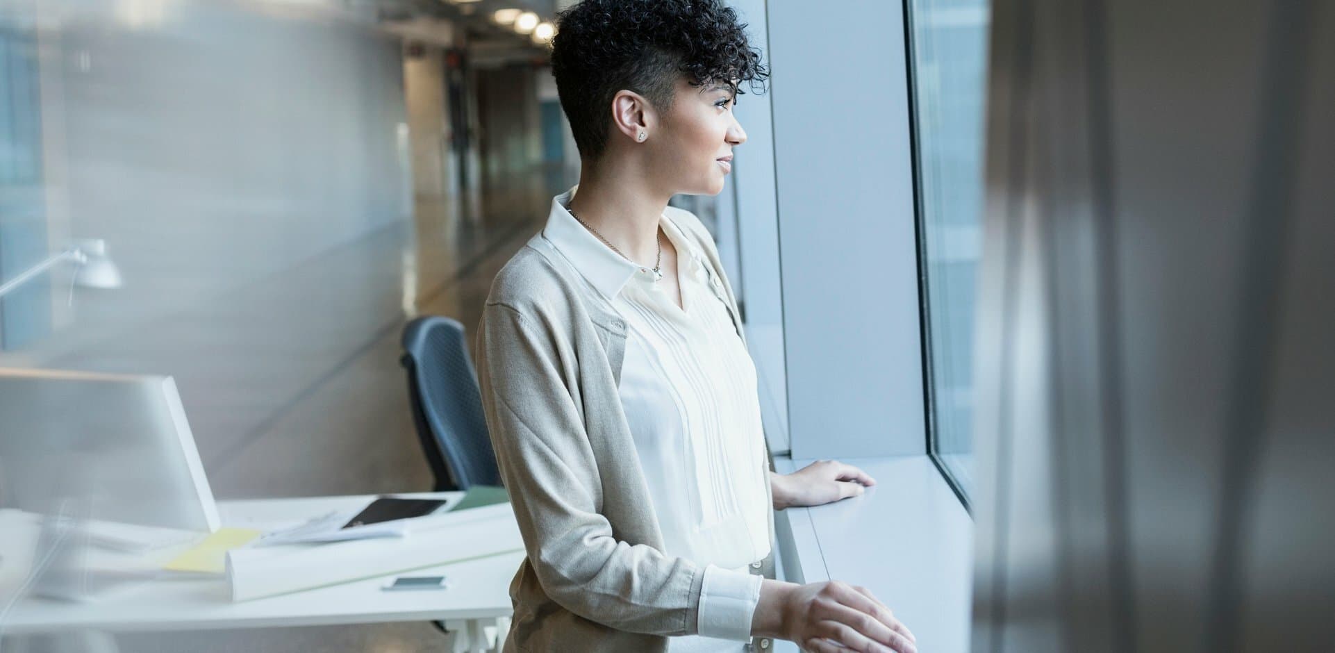 person standing by an office window thinking