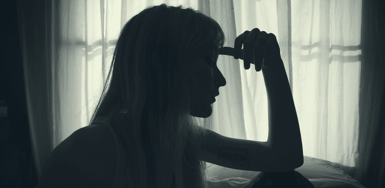 person sitting in a dark room with their hand on their forehead
