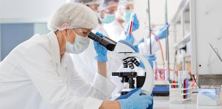 Scientists wearing protective gear looking through microscope