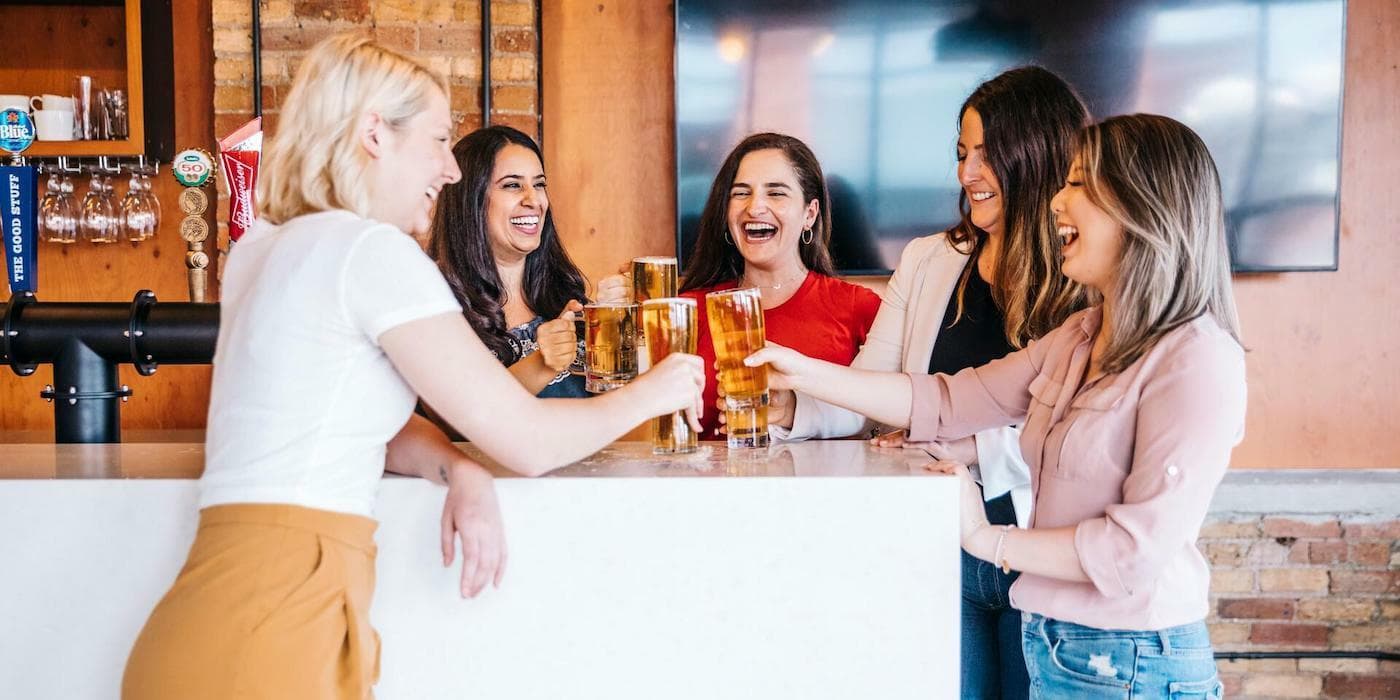 a group of people gathered around an office bar, clinking beer glasses