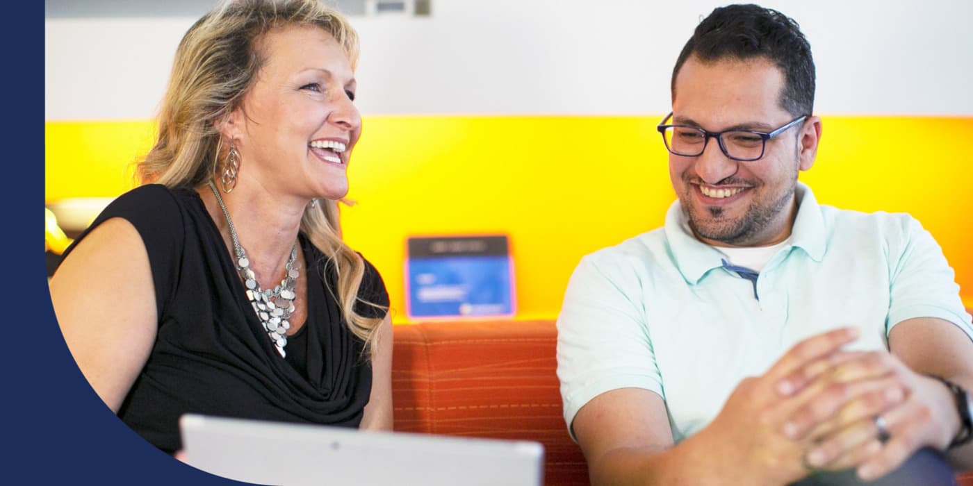 Two Avanade employees sitting on a couch with a tablet and laughing.