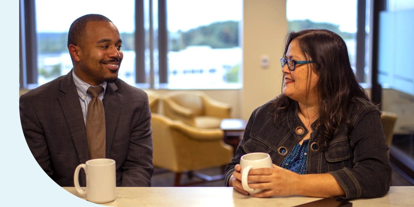 Two First Citizens Bank employees in a conference room, sitting at a countertop with coffee cups.