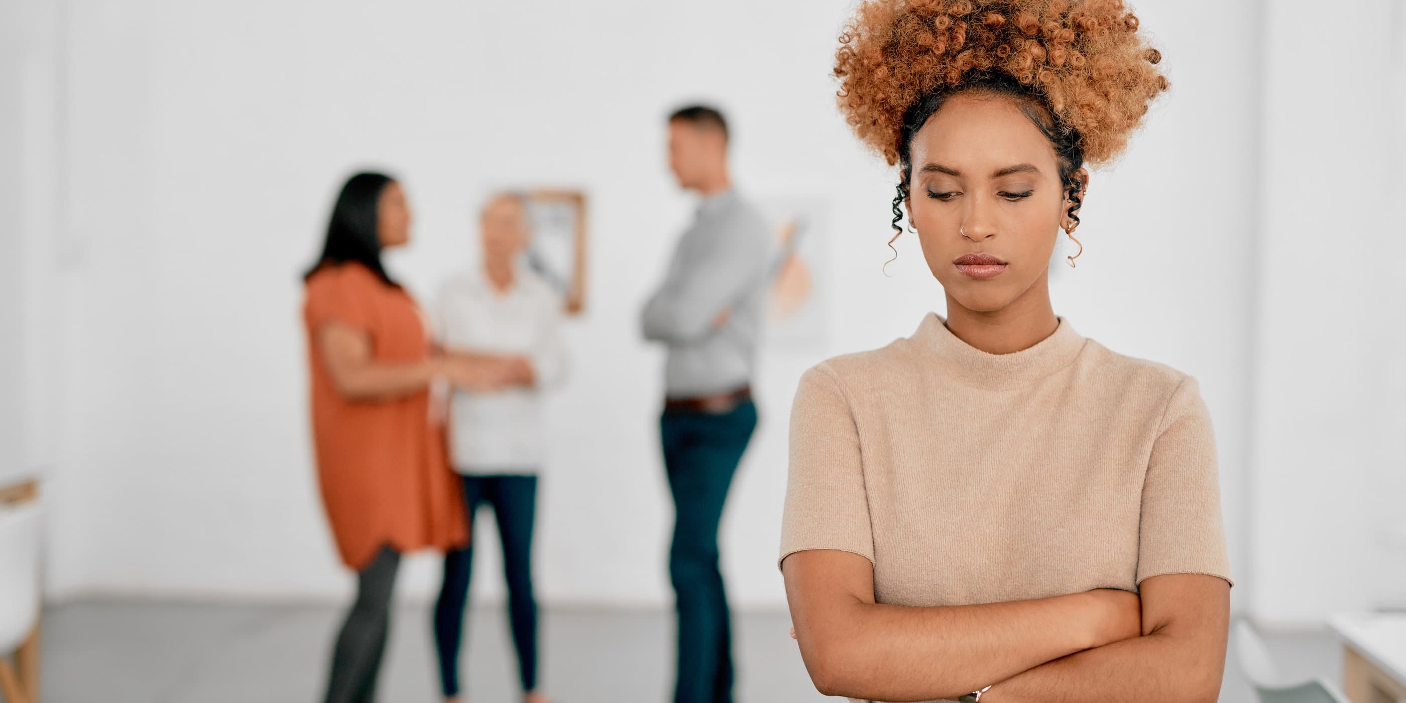 sad person standing with arms crossed with group of coworkers in the background