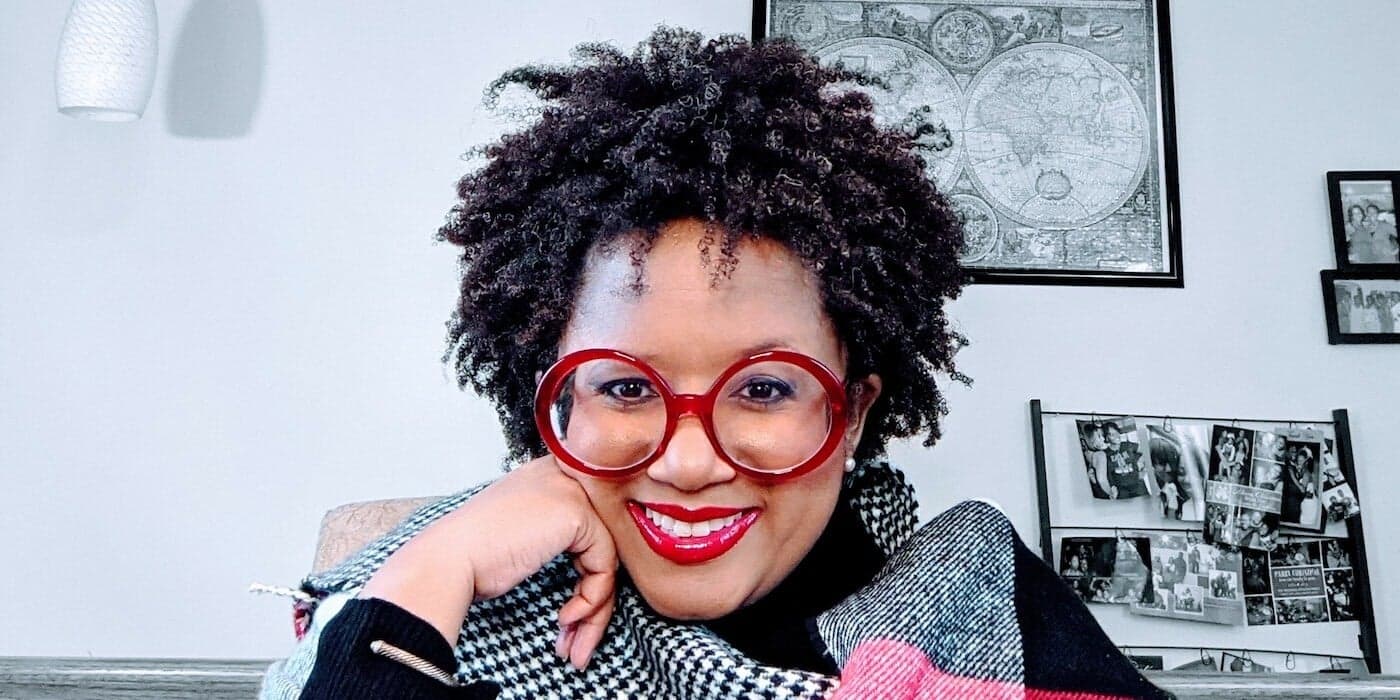 person with short black hair wearing red-rimmed glasses and red lipstick