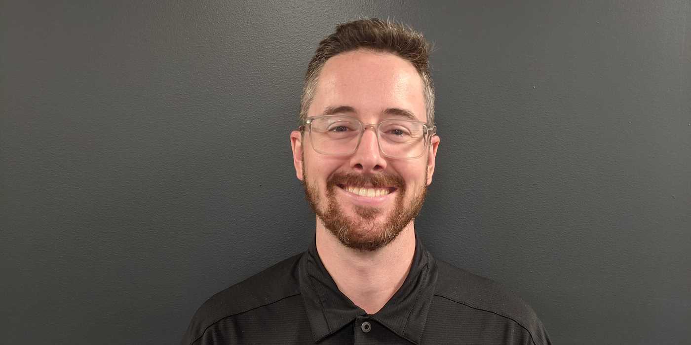 person with a beard and glasses against a grey background