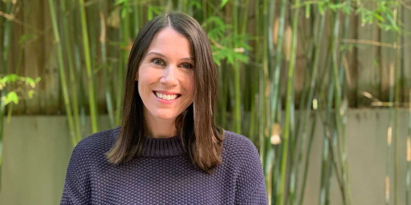 person with long brown hair standing outside in front of a bamboo wall