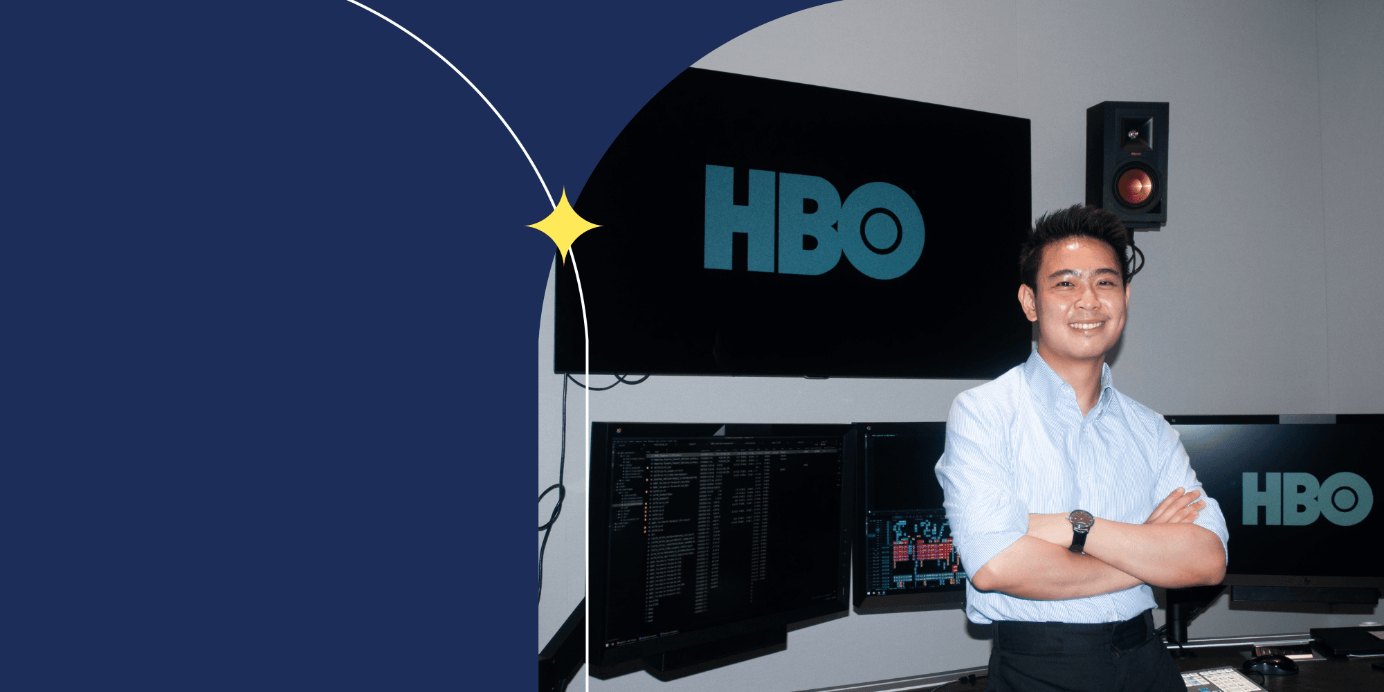 A person dressed in a light blue shirt and facing the camera. They are smiling and have their arms crossed. A screen with the word "HBO" is behind them.