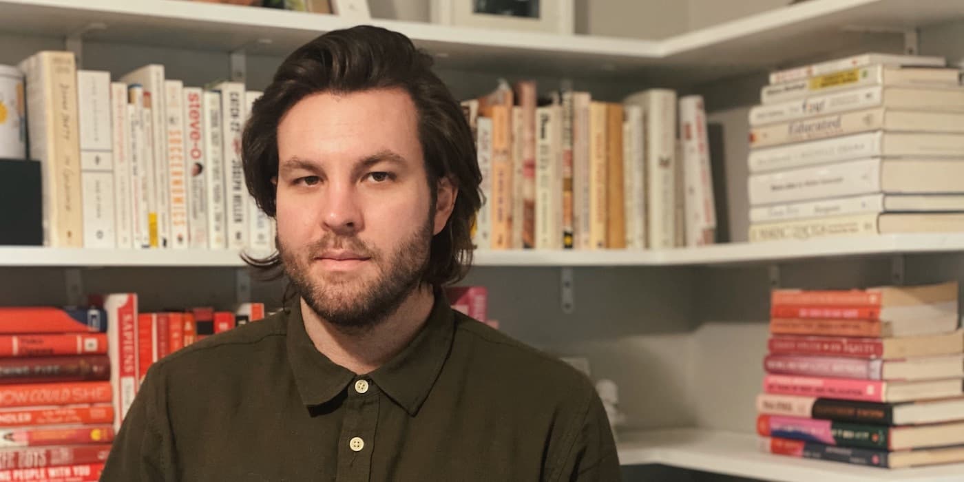 person in a collared shirt sitting in front of shelves stacked with books