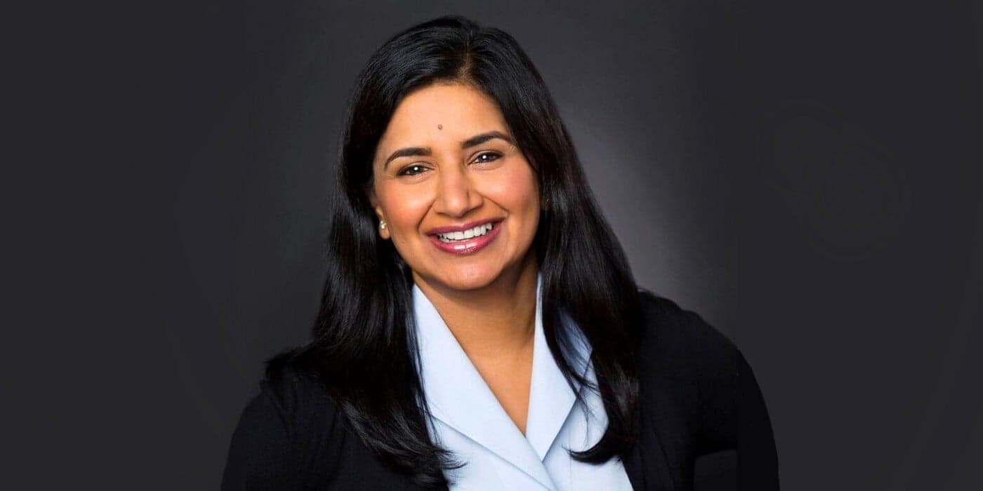 smiling person with long black hair against a dark grey background