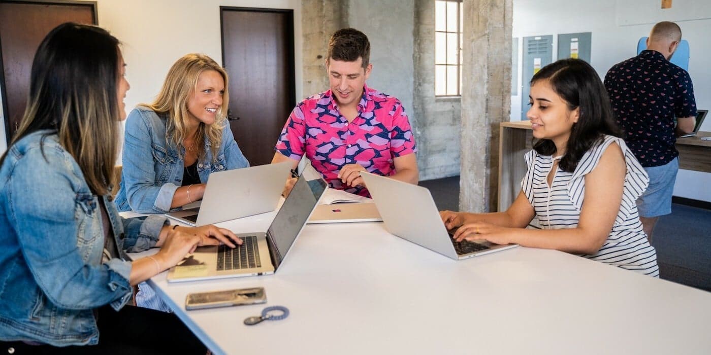 employees working on their laptops while sitting together at a communal table in an office