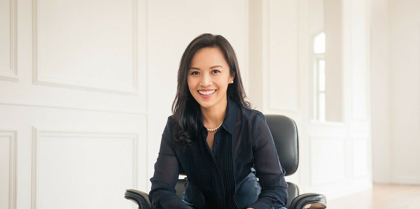person with long hair sitting in a desk chair with a white wall in the background