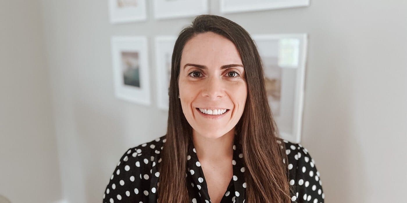 a person with long brown hair and a polka dot shirt smiling in front of a wall with framed photos