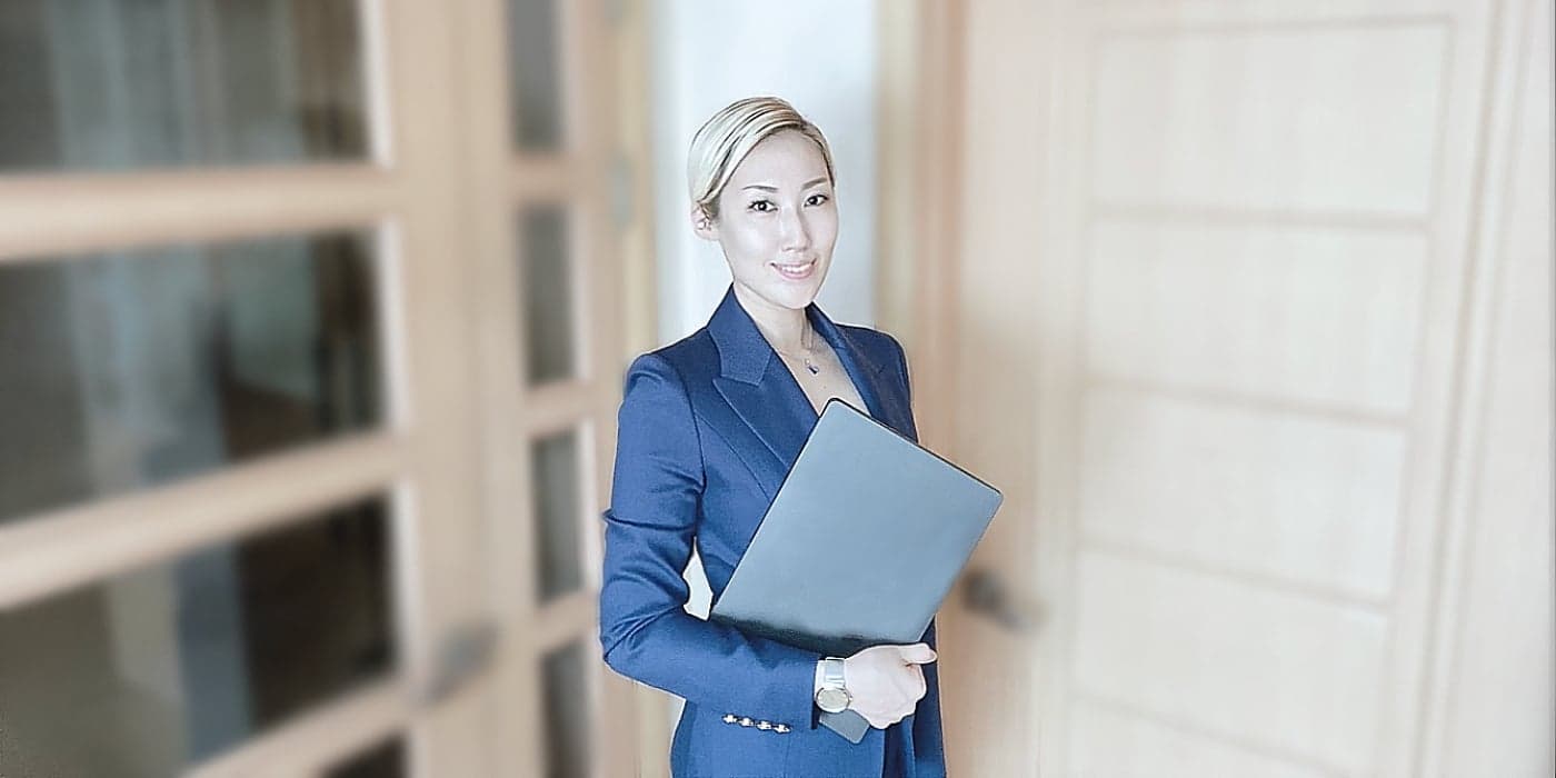 a person with short blonde hair wearing a blazer and holding a laptop