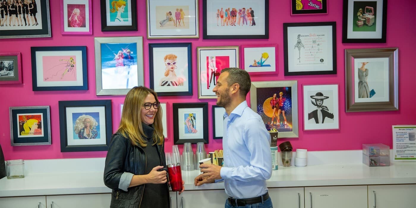 Two people talking while drinking coffee in an office break room.