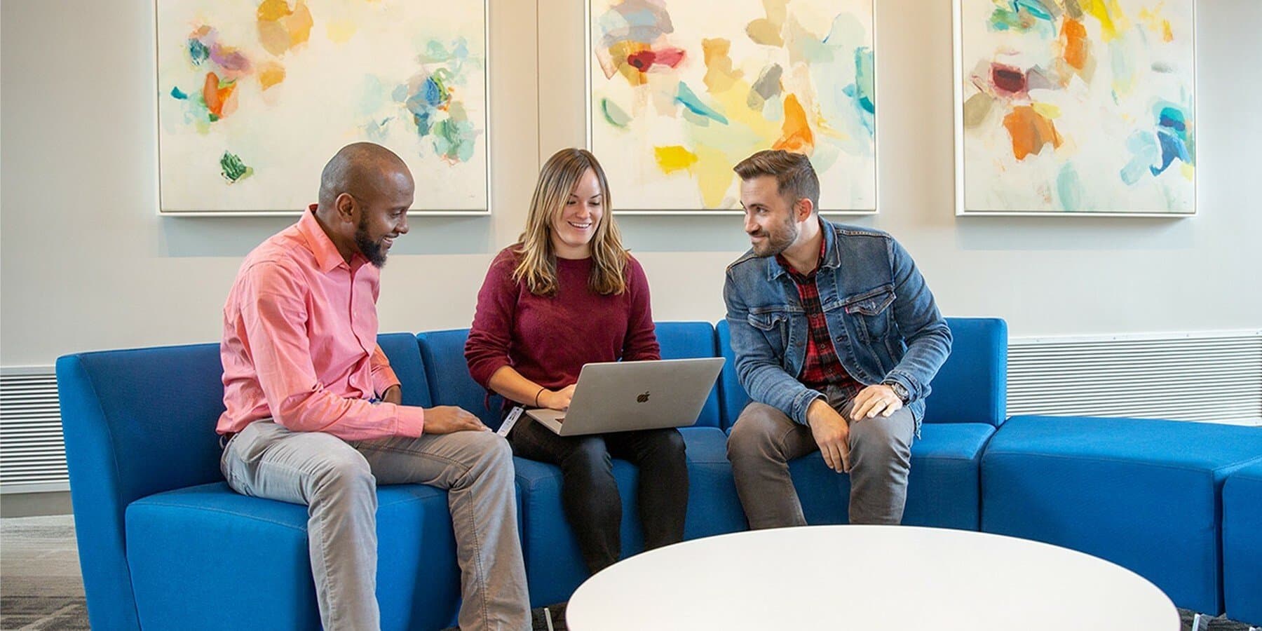 three employees gathered in front of a laptop at the office.