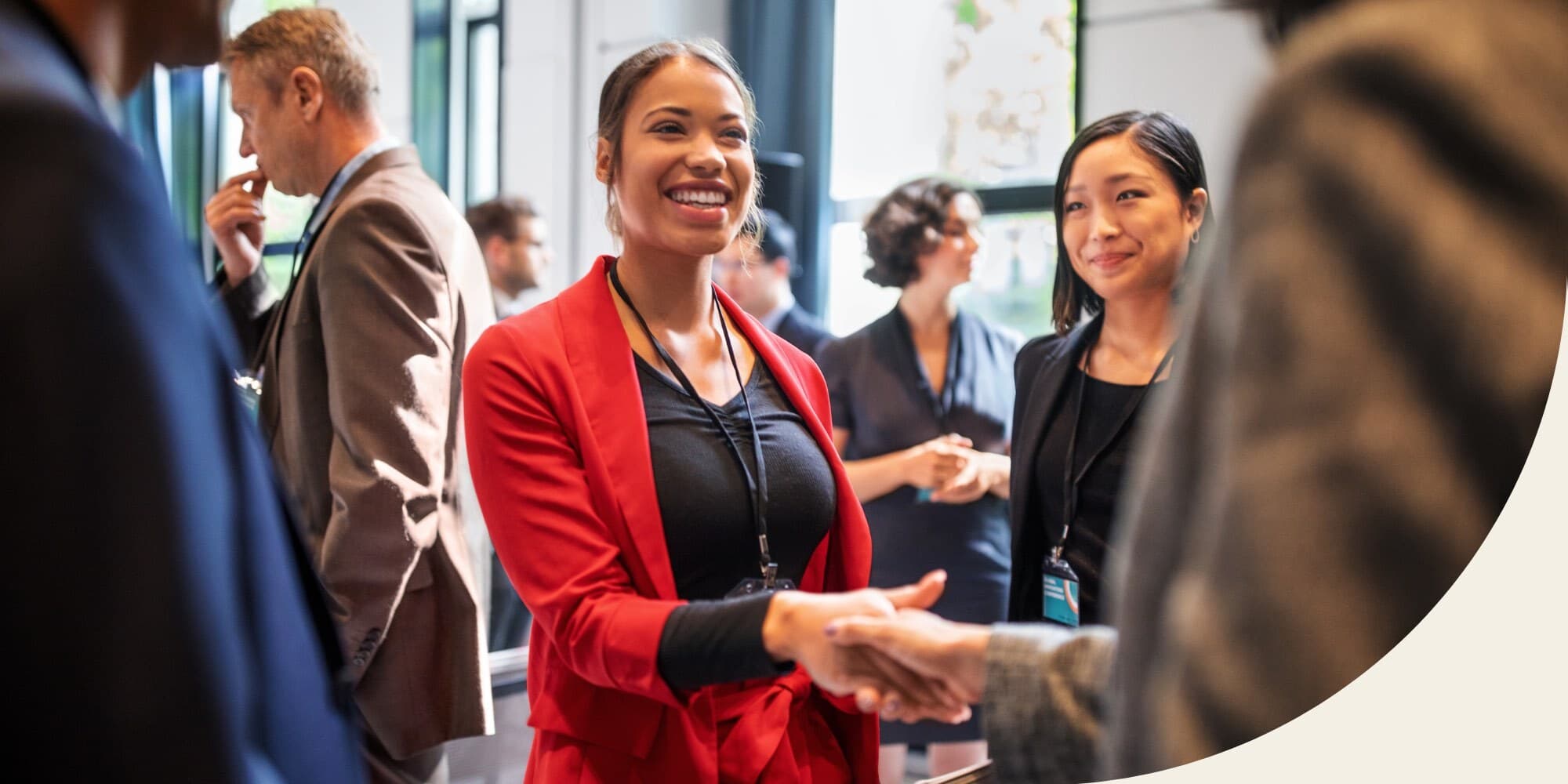 person smiling and shaking someone's hand at a networking event with other attendees visible in the background and foreground