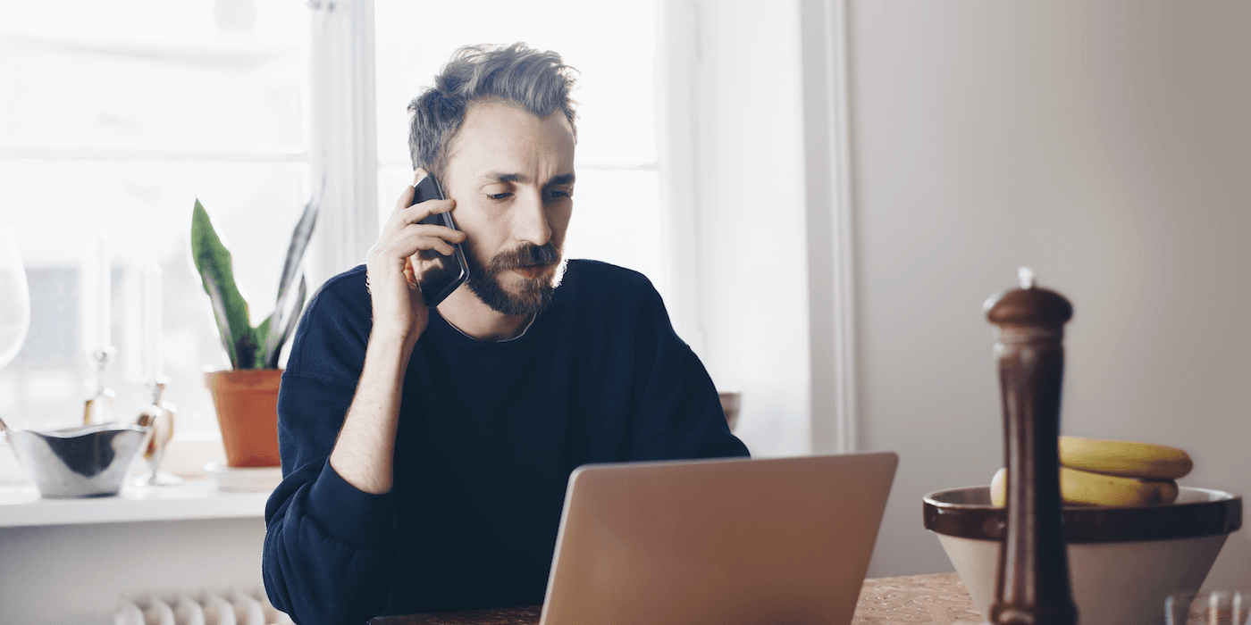 person sitting at kitchen table in front of laptop talking on cell phone