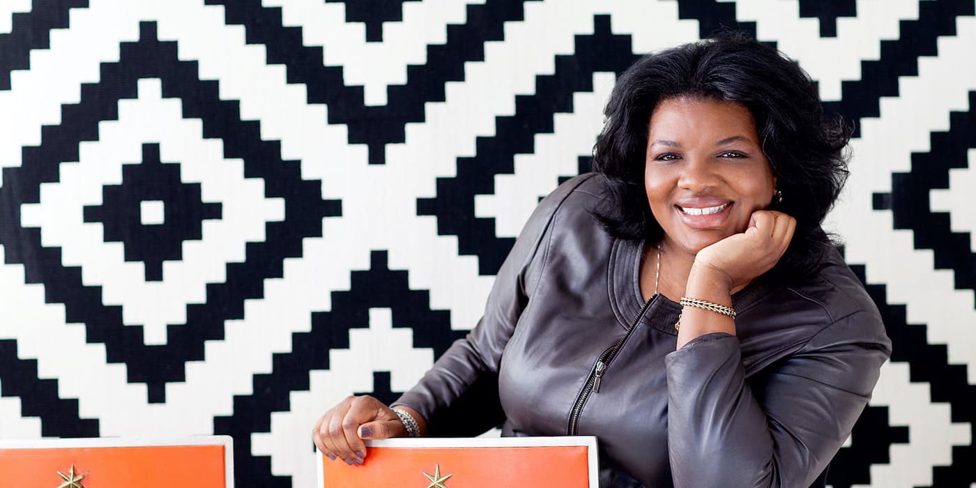 person smiling with their hand under their chin sitting in front of a black-and-white patterned wall