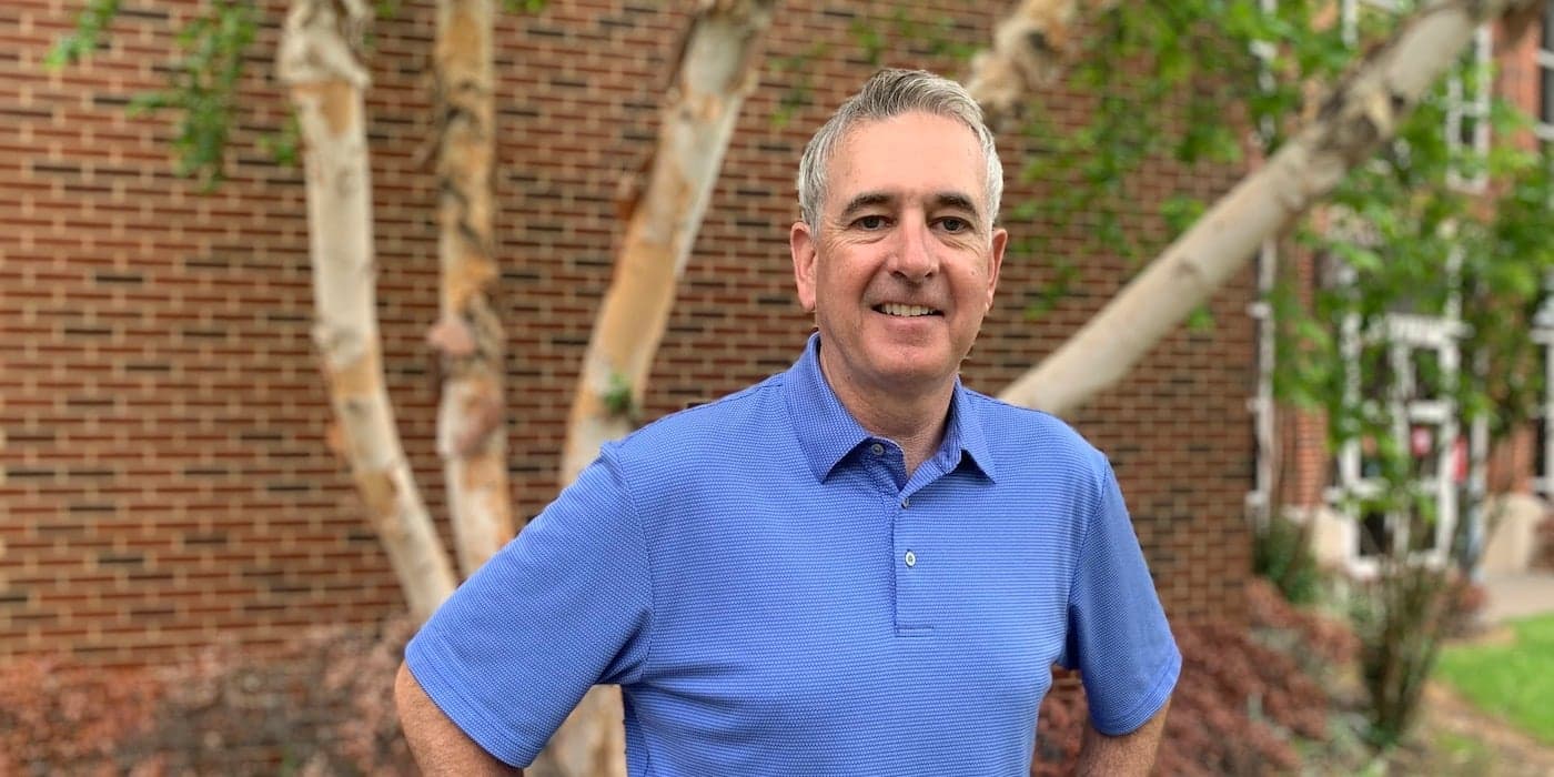 person wearing a blue polo shirt standing in front of a tree.