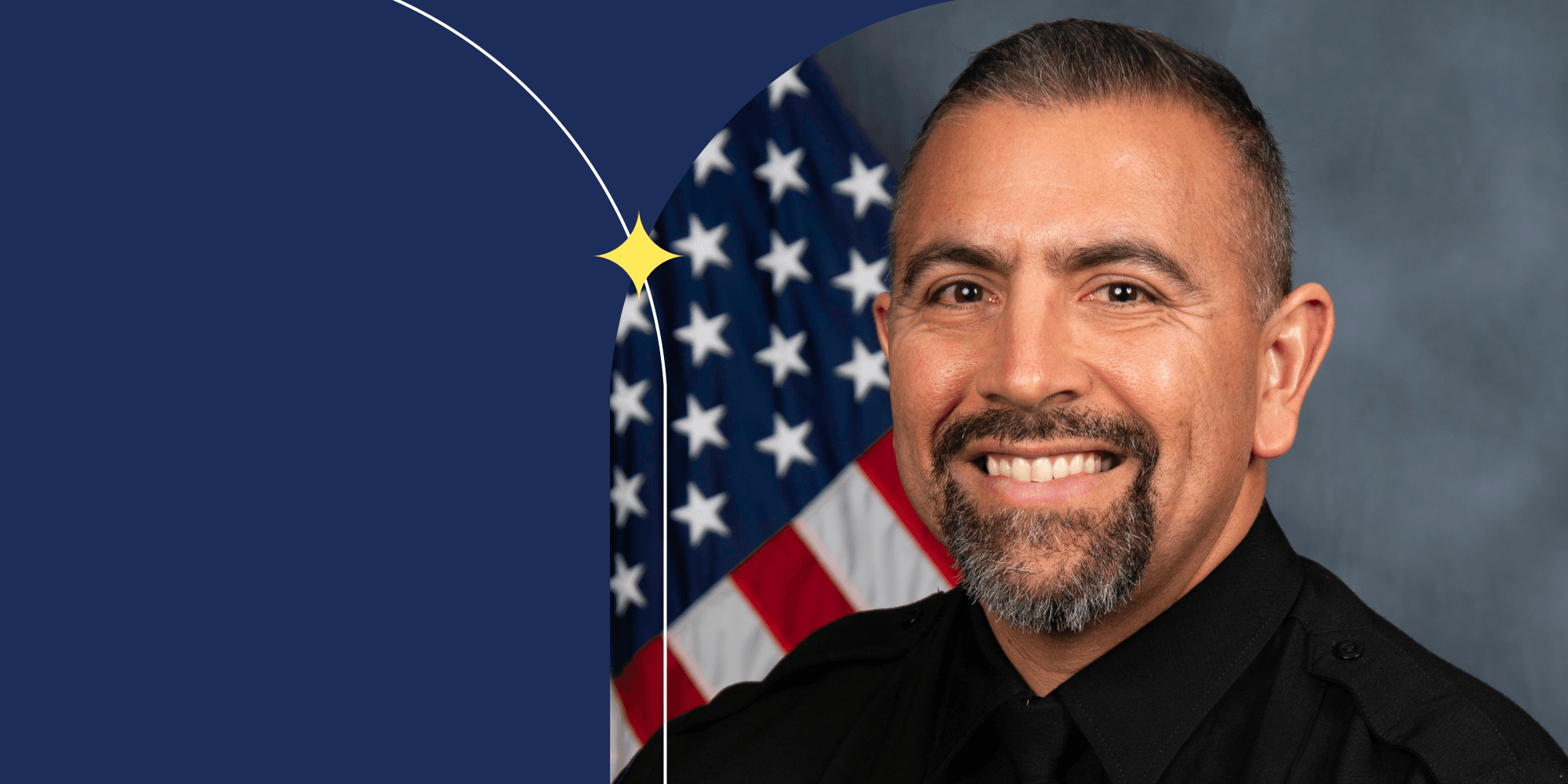 A smiling person who is dressed in a black shirt and facing the camera. An American flag can be seen behind them.