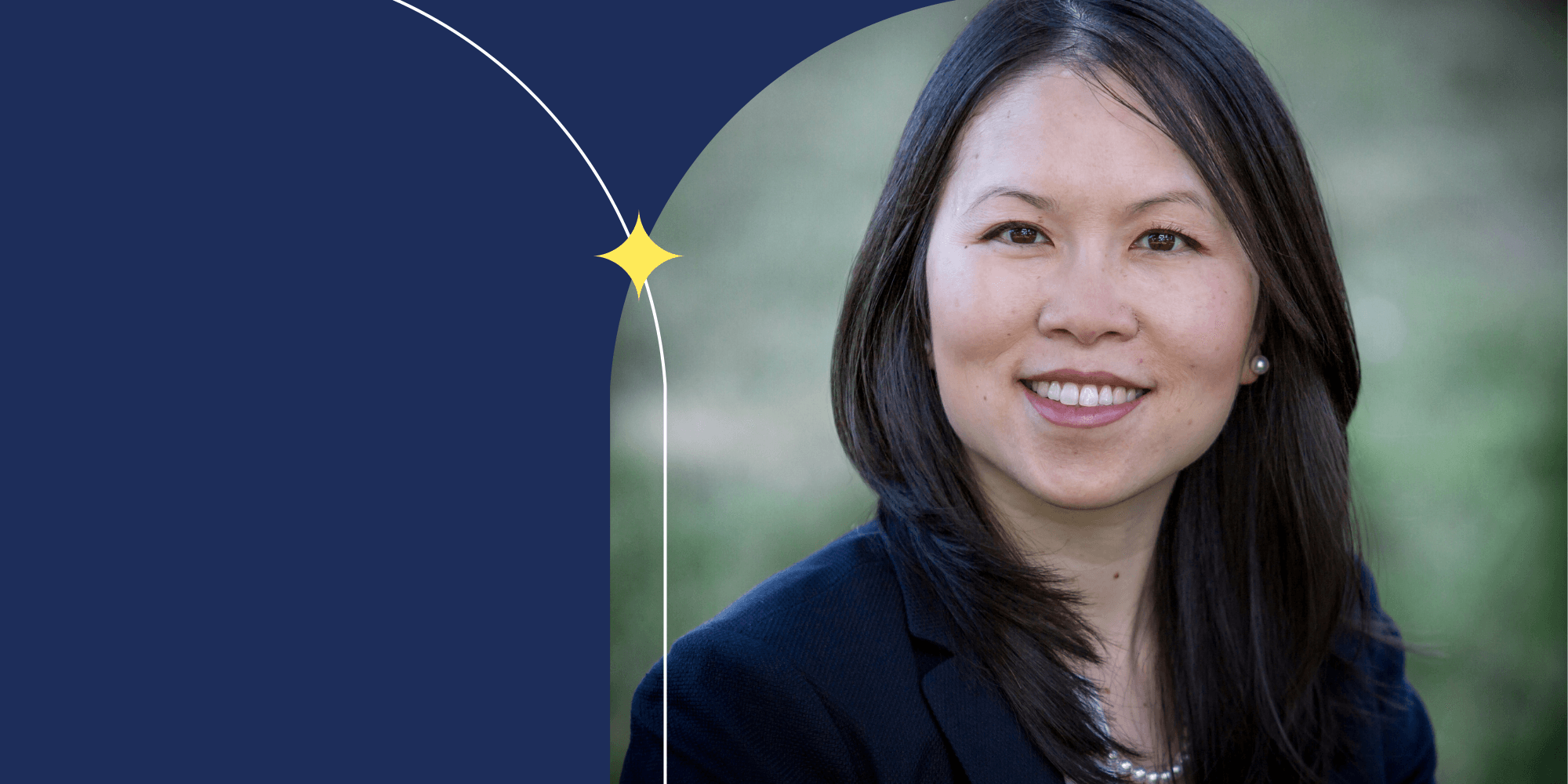 A person smiling and facing the camera. They are dressed in a blue blazer and wear a pearl necklace.