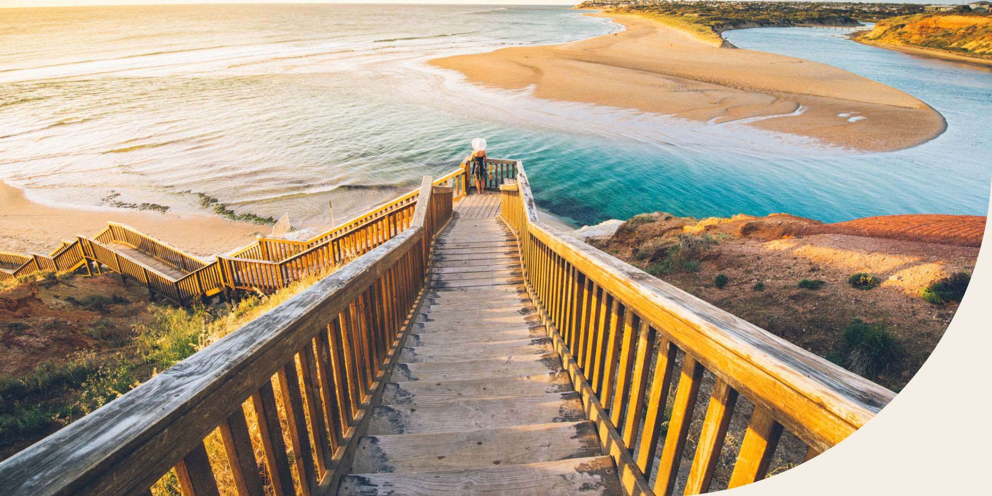 wooden stairs leading down to beach of sand and water with a person visible at the bottom of the steps