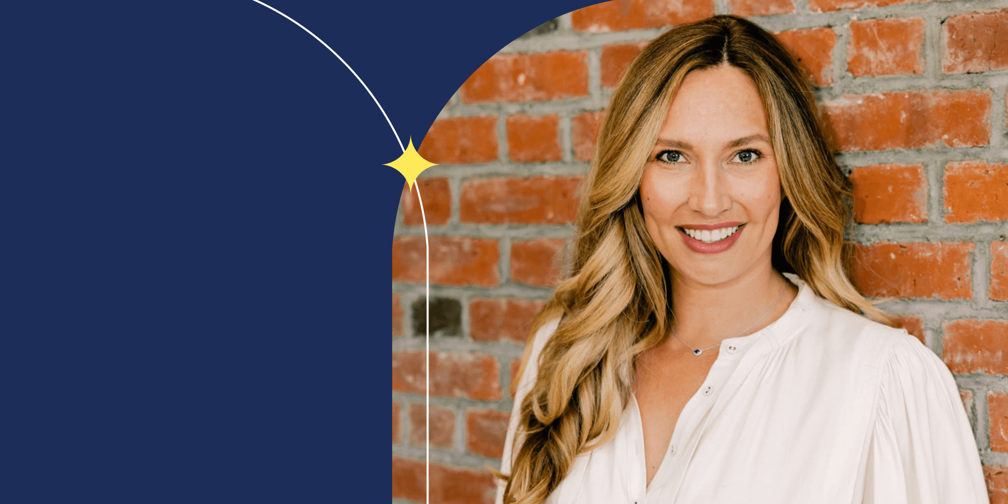 A smiling person facing the camera. They wear a white dress shirt and a necklace. They have long hair.