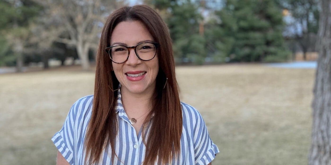 person with glasses and long hair standing outside with trees in the background