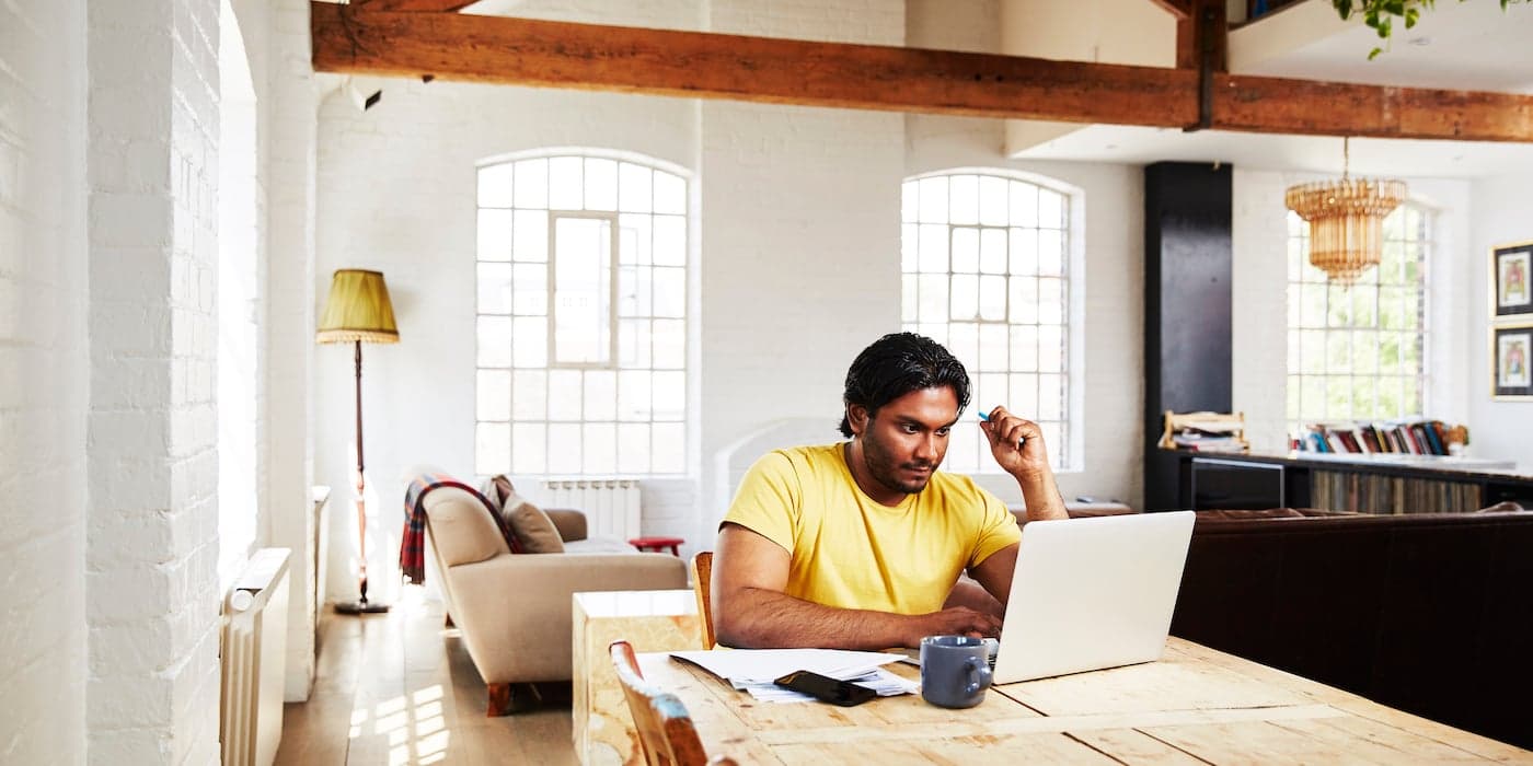 person sitting at a dining table at home working on a laptop
