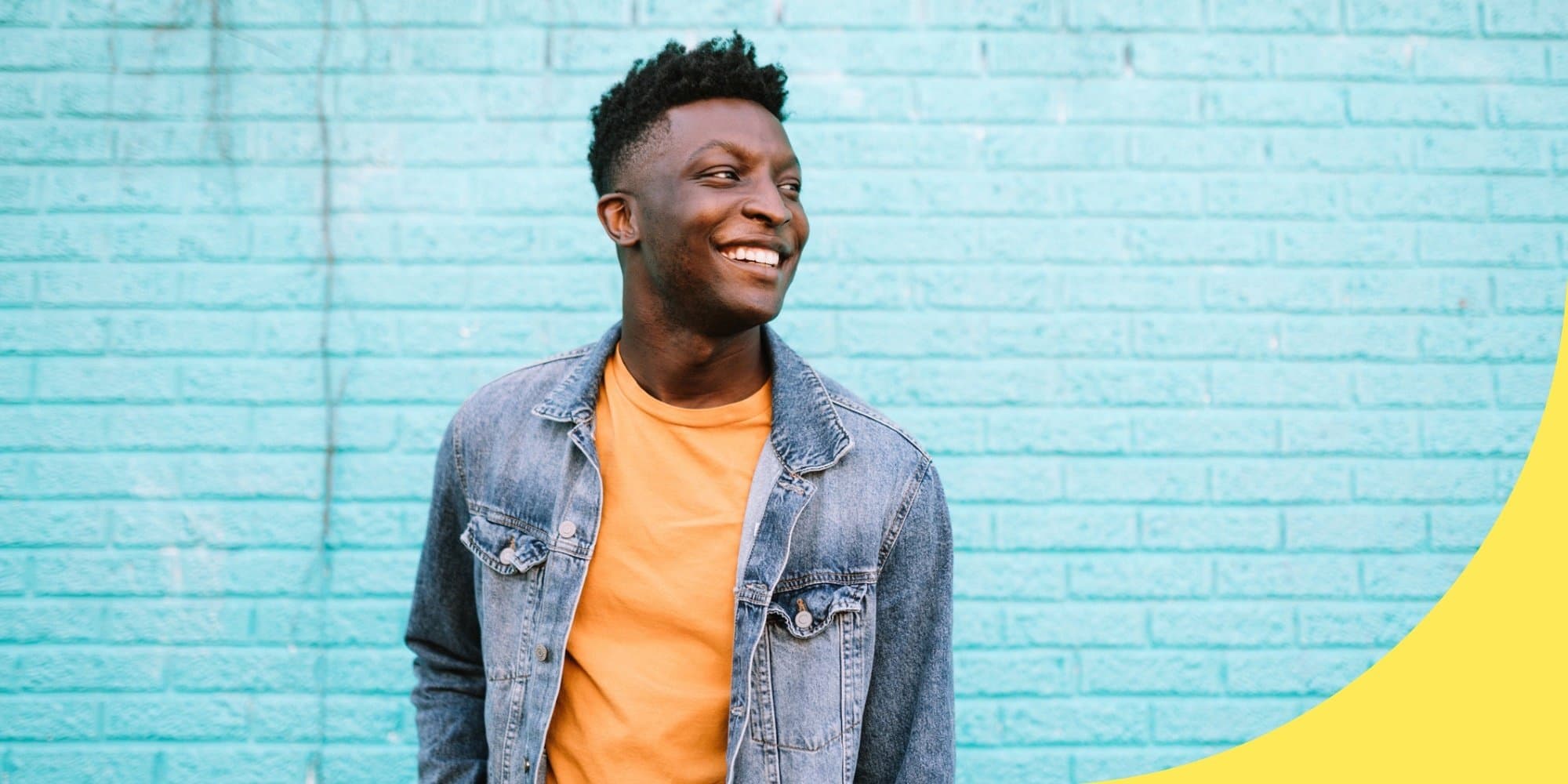 person standing in front of a light blue brick building smiling and looking off to the side