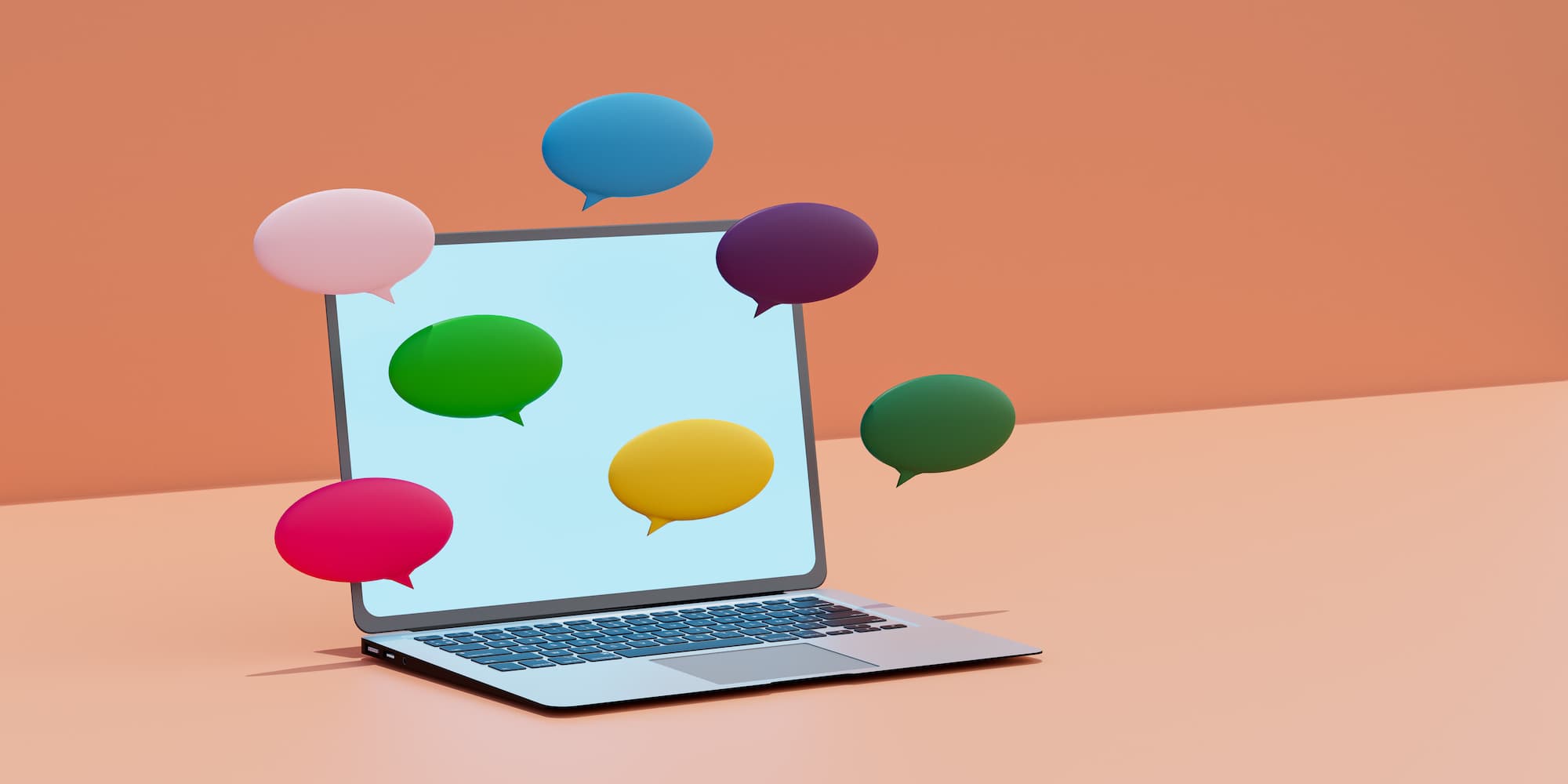 laptop with colored speech bubbles on and around the screen on a light peach surface in front of darker peach-colored wall