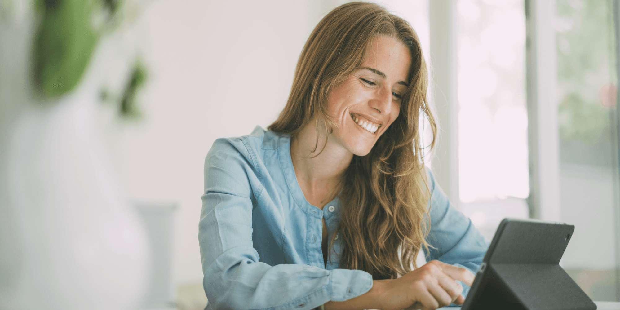 person sitting down and smiling as they use the touch screen on a tablet propped up in front of them