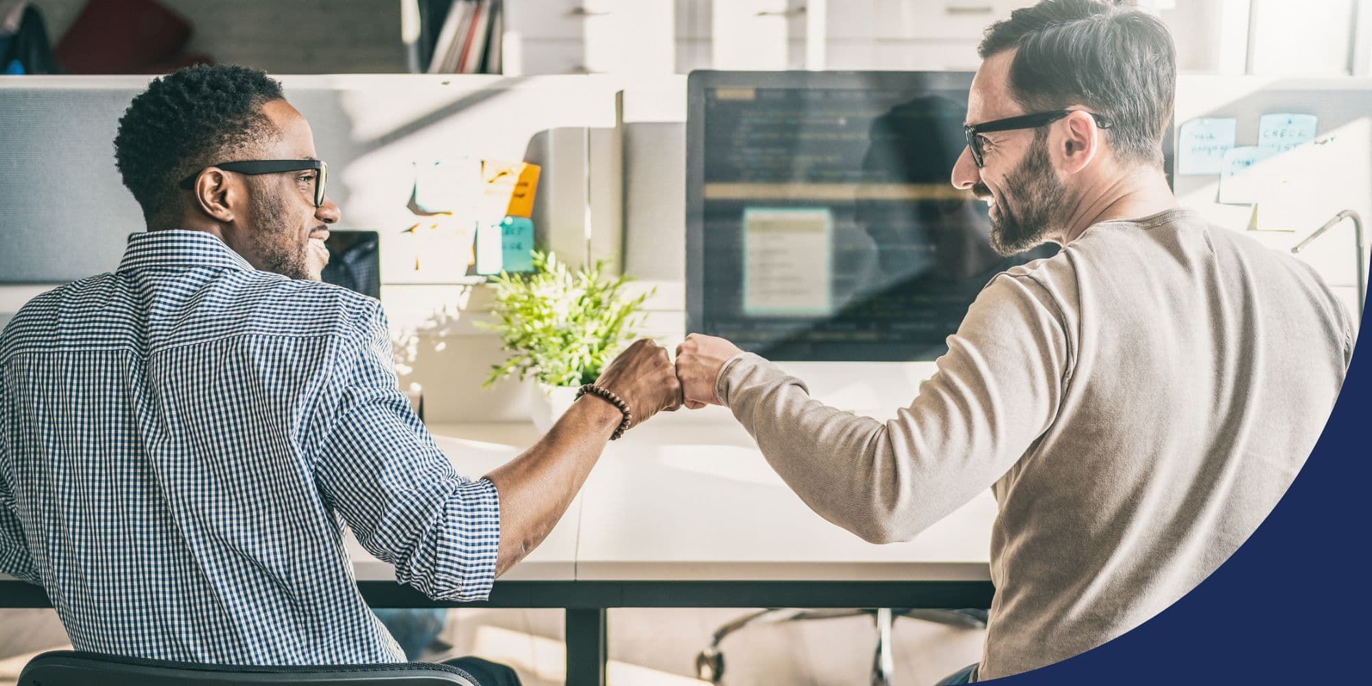 two people doing a fist bump while working on computers in a white open office