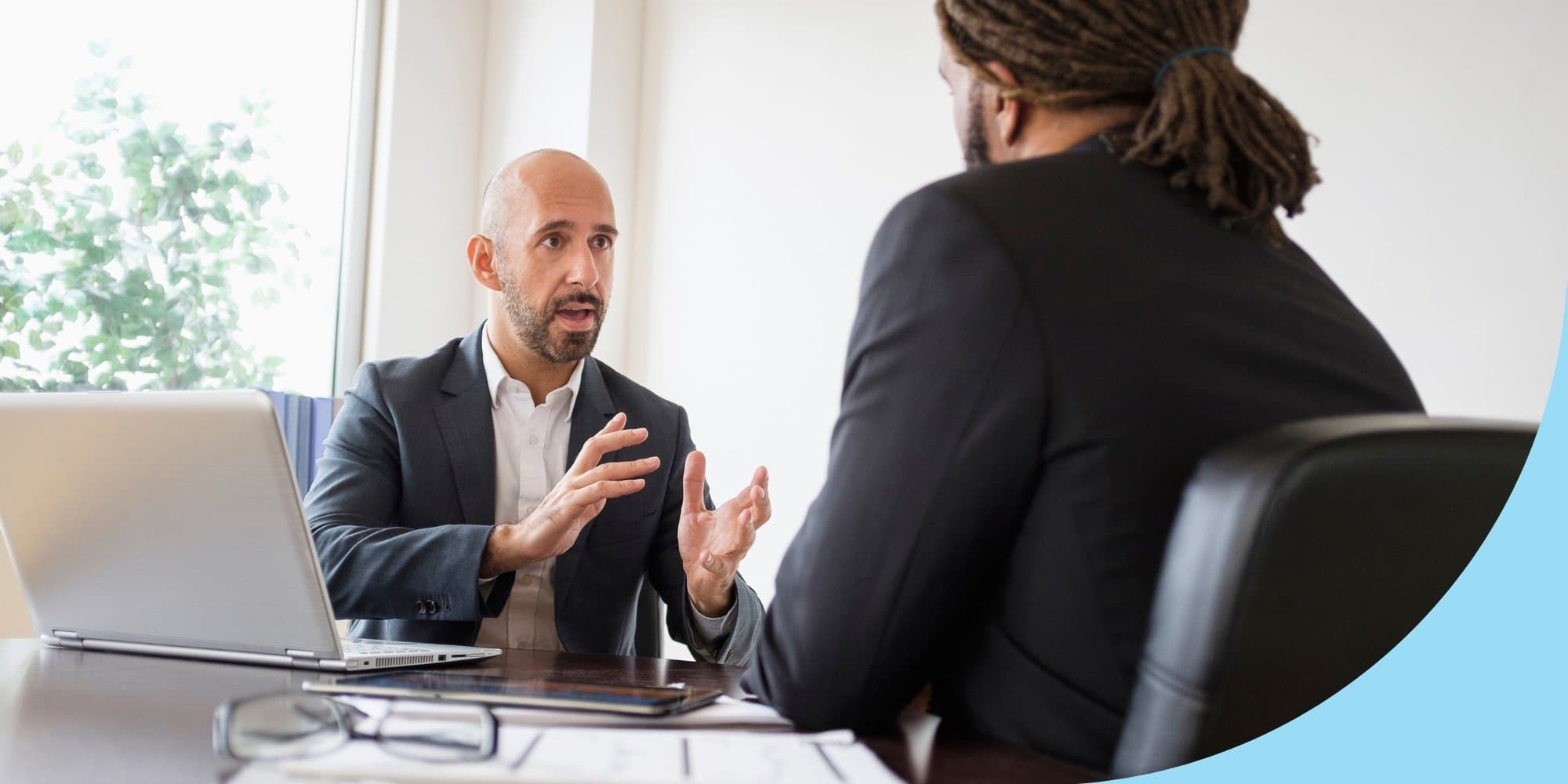 two people in white conference room talking, one person facing the camera answering an interview question