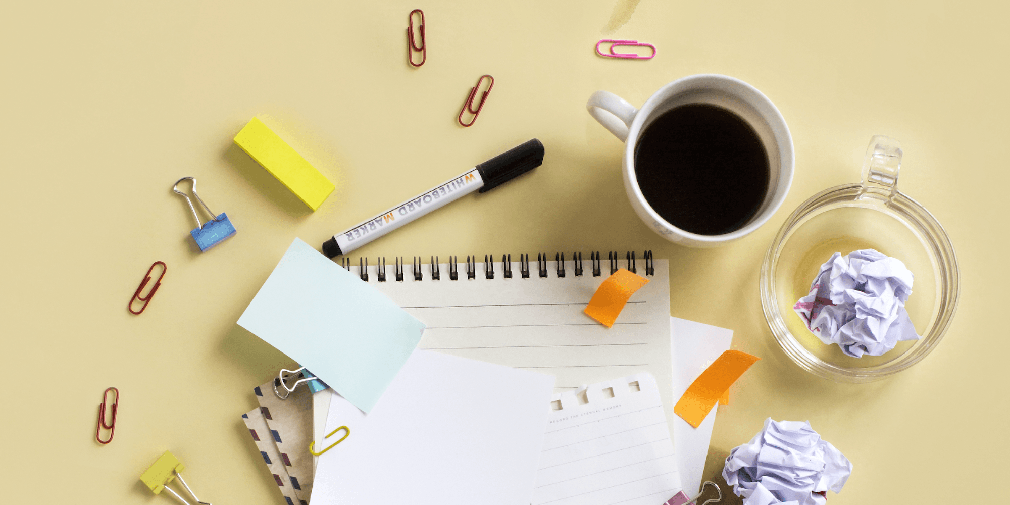 aerial shot of messy workspace with notepad, crumpled papers, paper clips, coffee cup, and more
